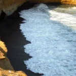 Arena volcánica rojiza de Playa Roja contrastando con las aguas turquesas del océano en Paracas