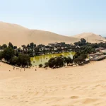 Oasis natural de Huacachina con palmeras y laguna rodeado de dunas gigantes de arena en Ica